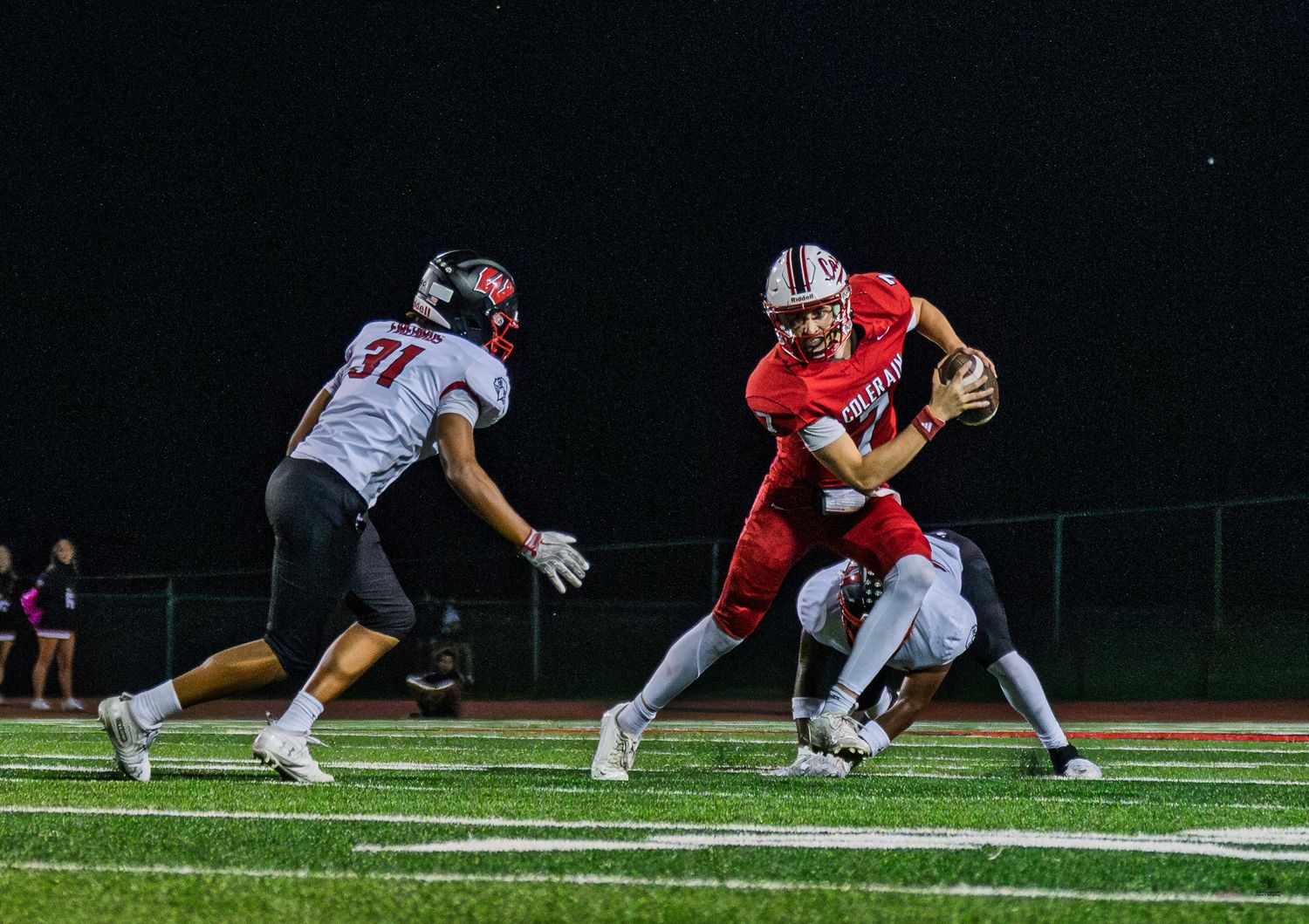 High school football player in red uniform breaks through tackle during night game on turf field.