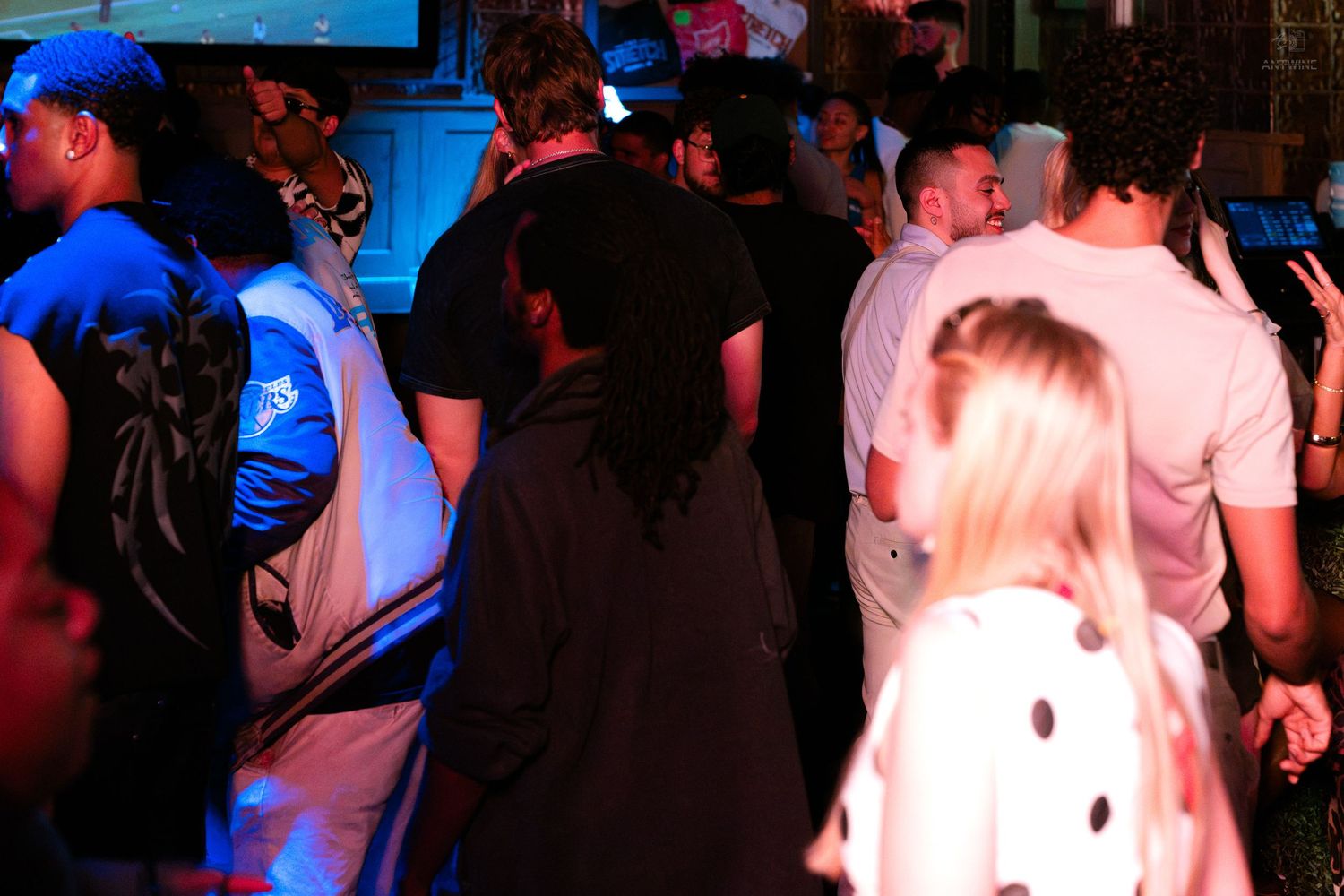 Crowd of partygoers dancing under blue lights at a busy nightclub.