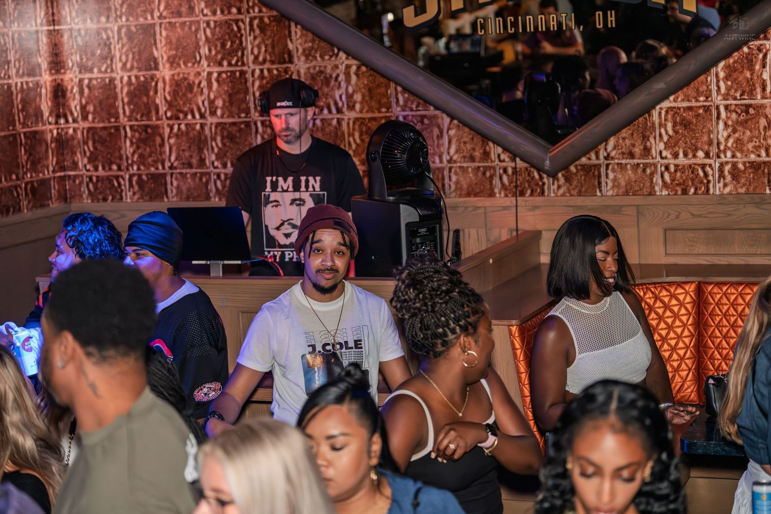 DJ performing at a nightclub while guests dance and socialize on the dance floor.