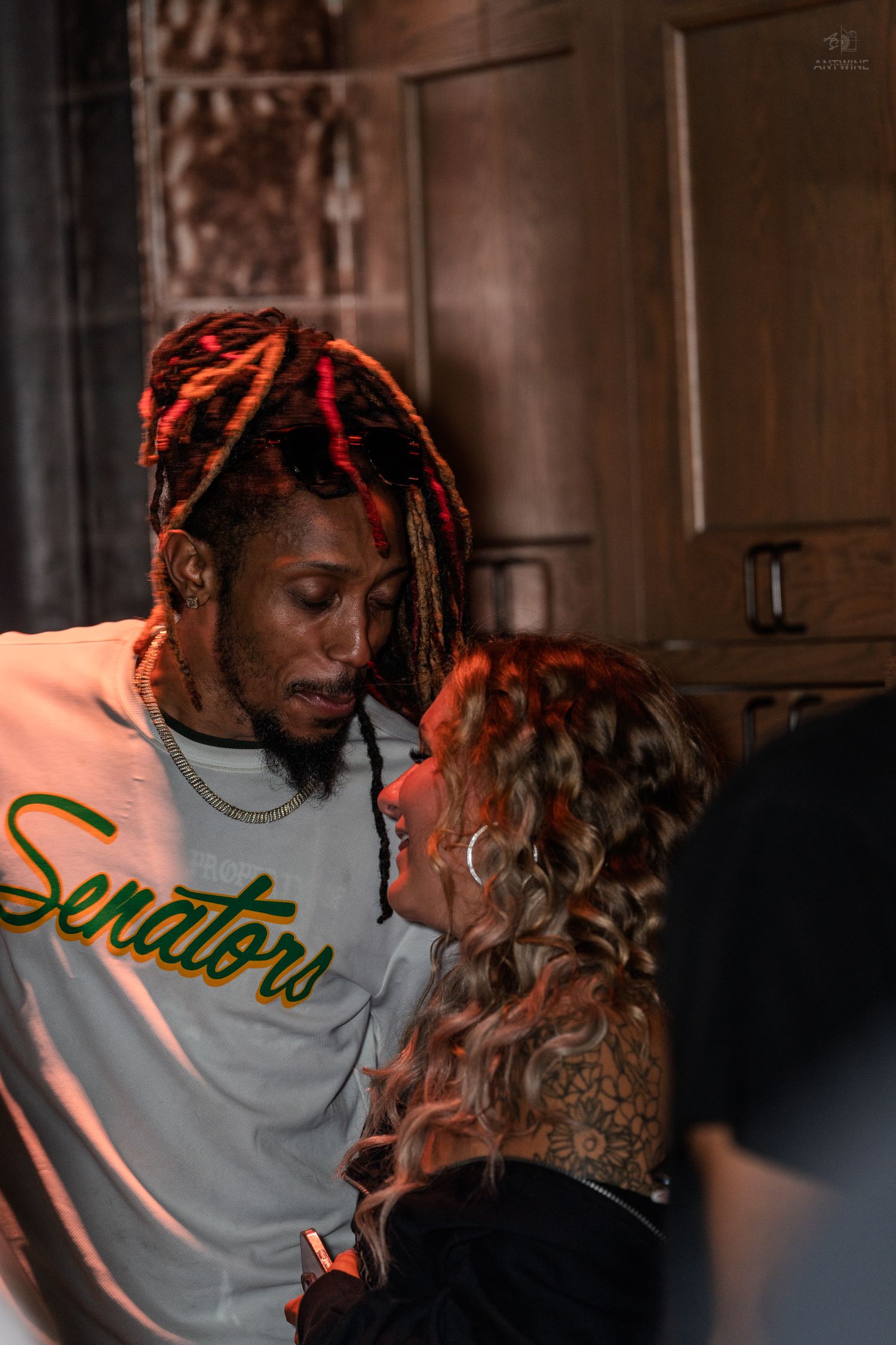 Man in Senators jersey with dreadlocks talking to a woman at a party.