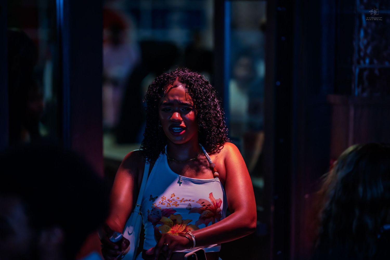 Woman with curly hair holding food under colorful nightclub lighting.