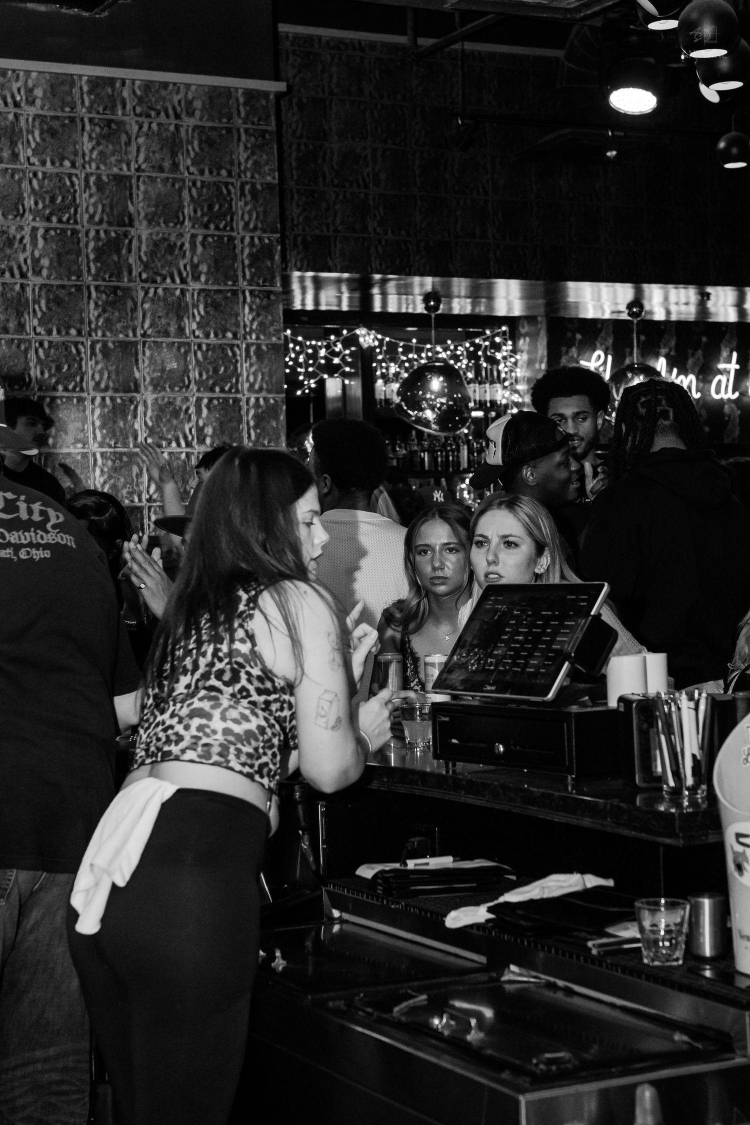 Black and white photo of women ordering drinks at a crowded nightclub bar.
