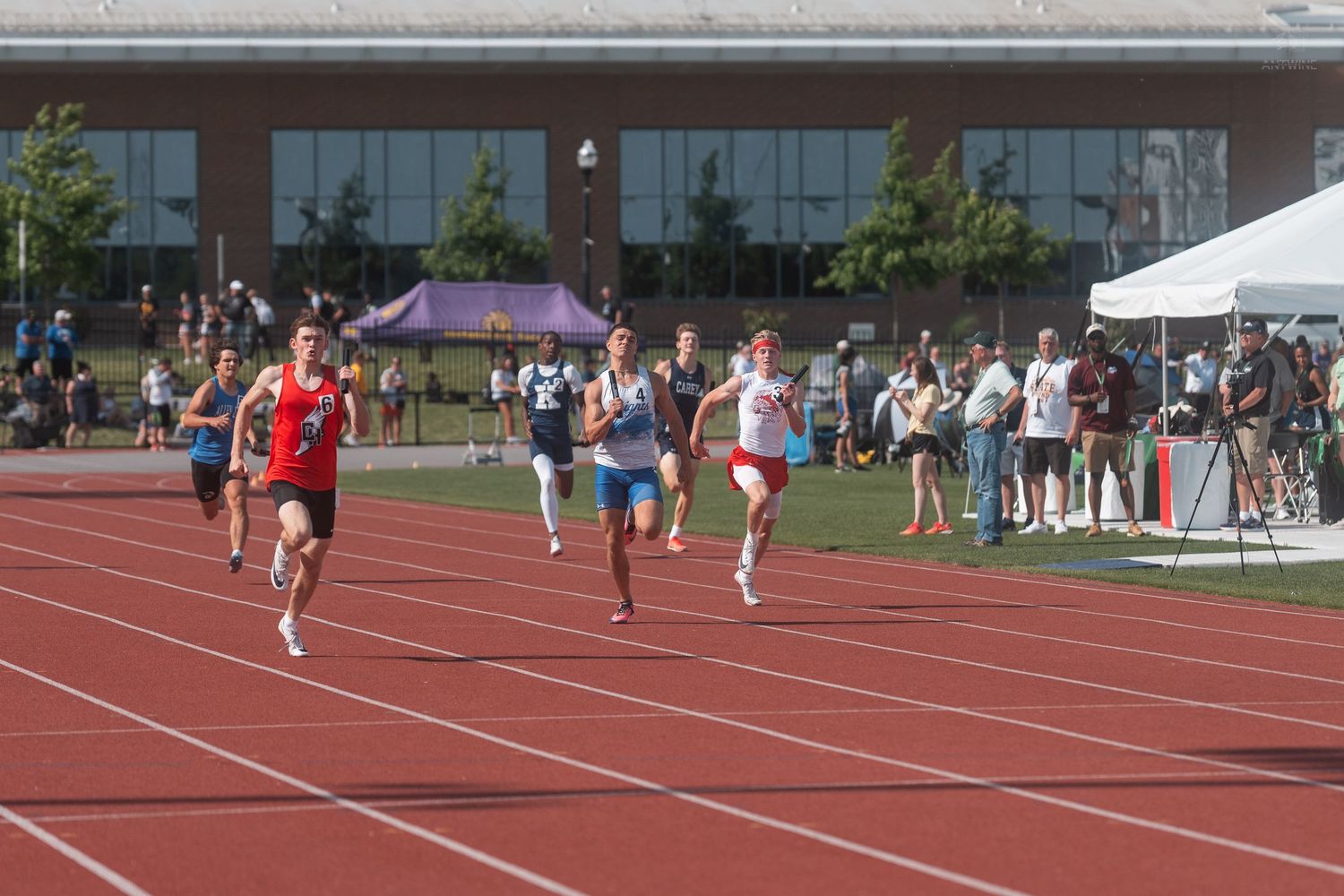 Male athletes sprint down the straightaway during a competitive high school track and field race.