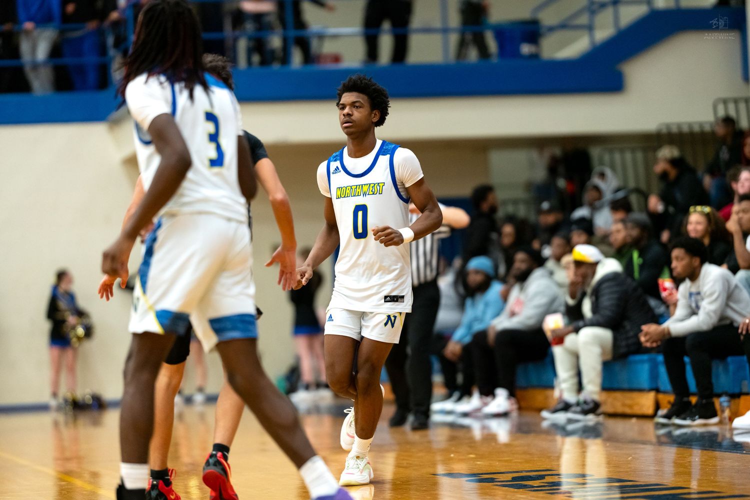 Basketball player wearing number 0 jersey walks on court during a high school game.