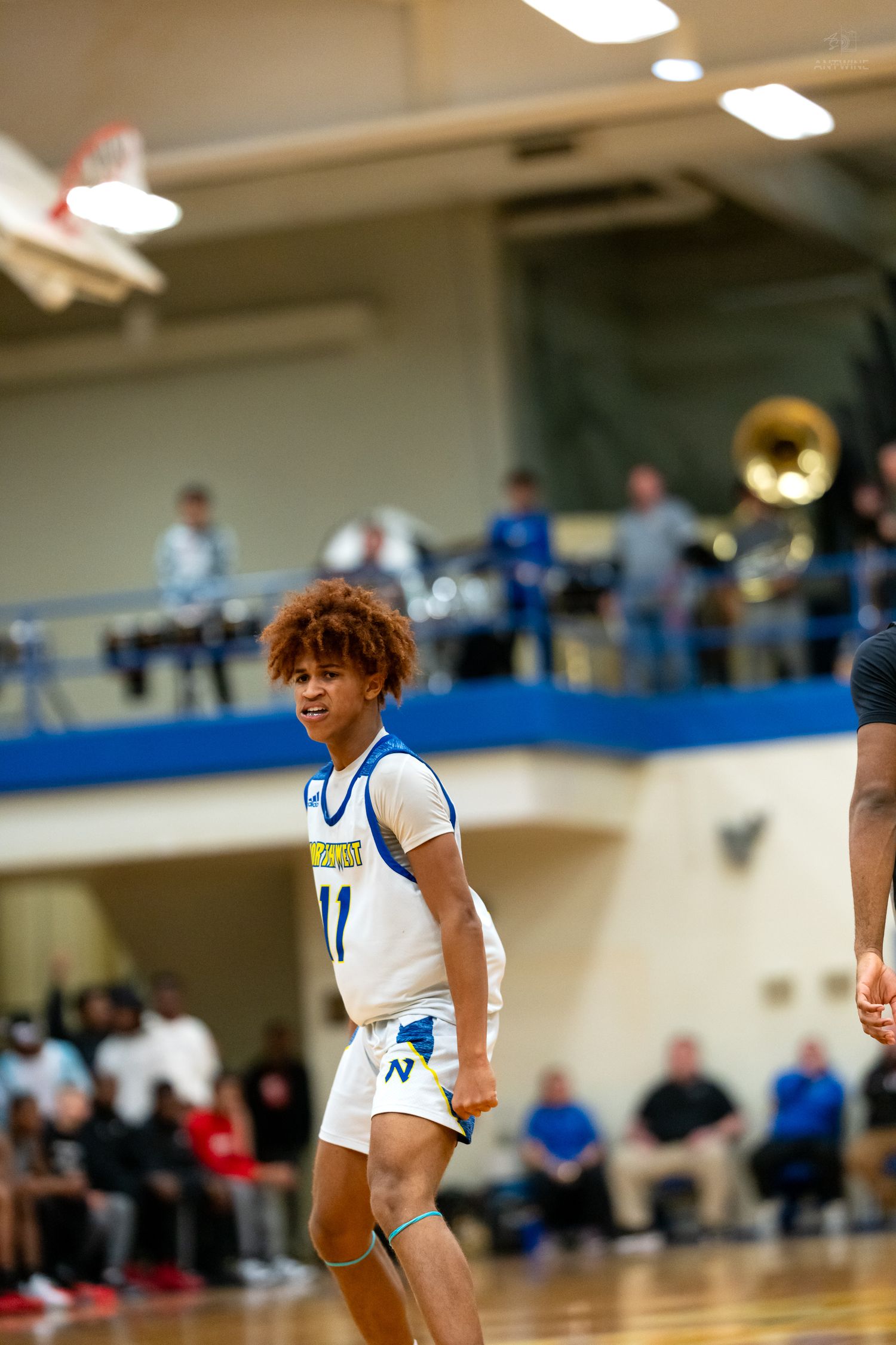 Young basketball player #11 in blue and white uniform walks on court with band visible in background.
