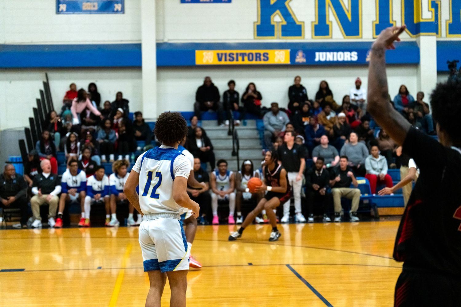 Player #12 in white sets up a play near half court during a high school basketball game.