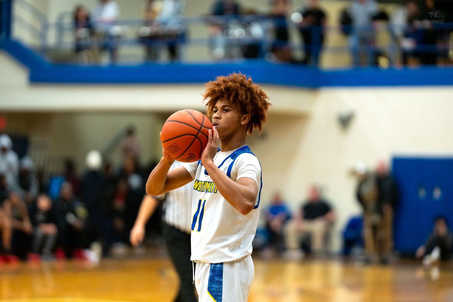 High school basketball player number 11 in white uniform prepares to shoot during an indoor gymnasium game.