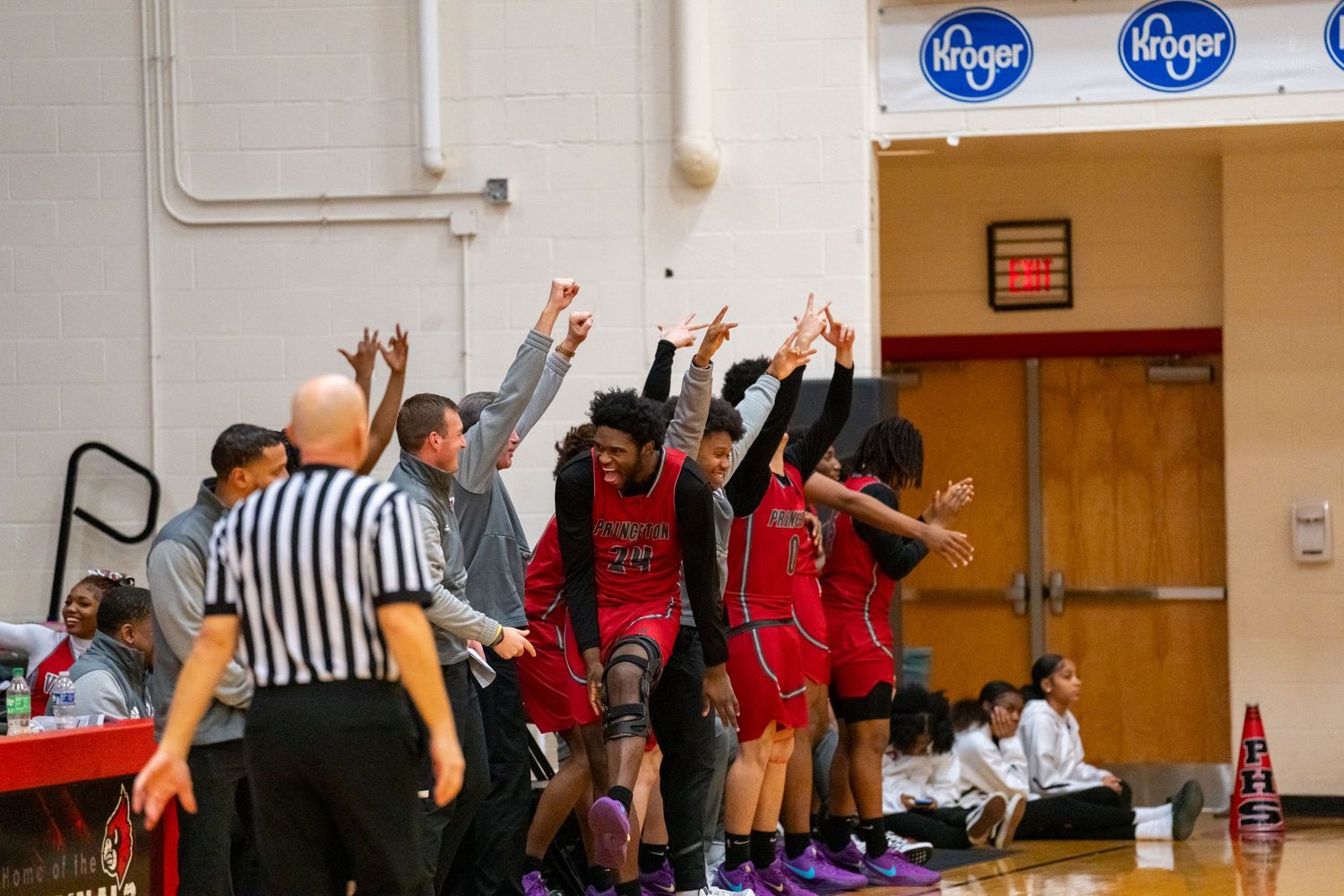 Red-uniformed basketball team bench erupts in celebration with hands raised during high school basketball game.