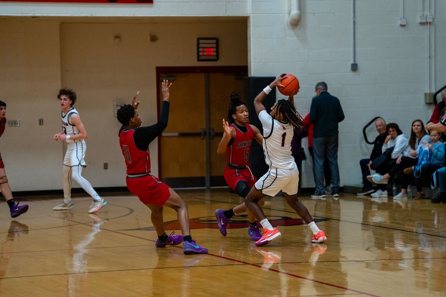 Basketball player number 1 attempts a pass while being defended by opponents in red jerseys.