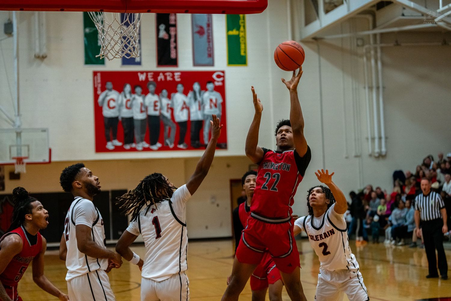 Red team player shoots over defenders during a competitive high school basketball game.