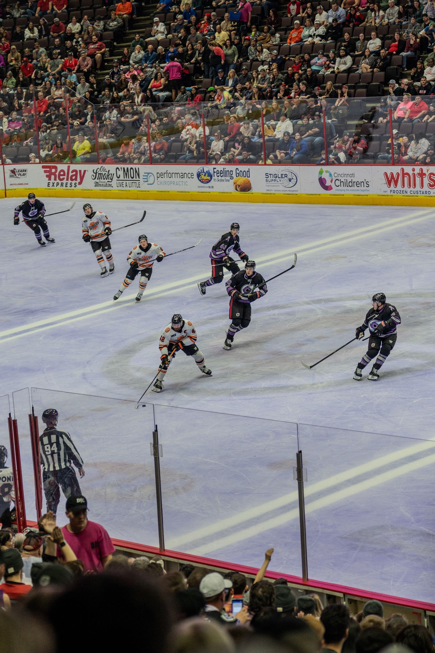 Professional ice hockey game action with players in navy and orange jerseys competing on indoor rink with crowd.