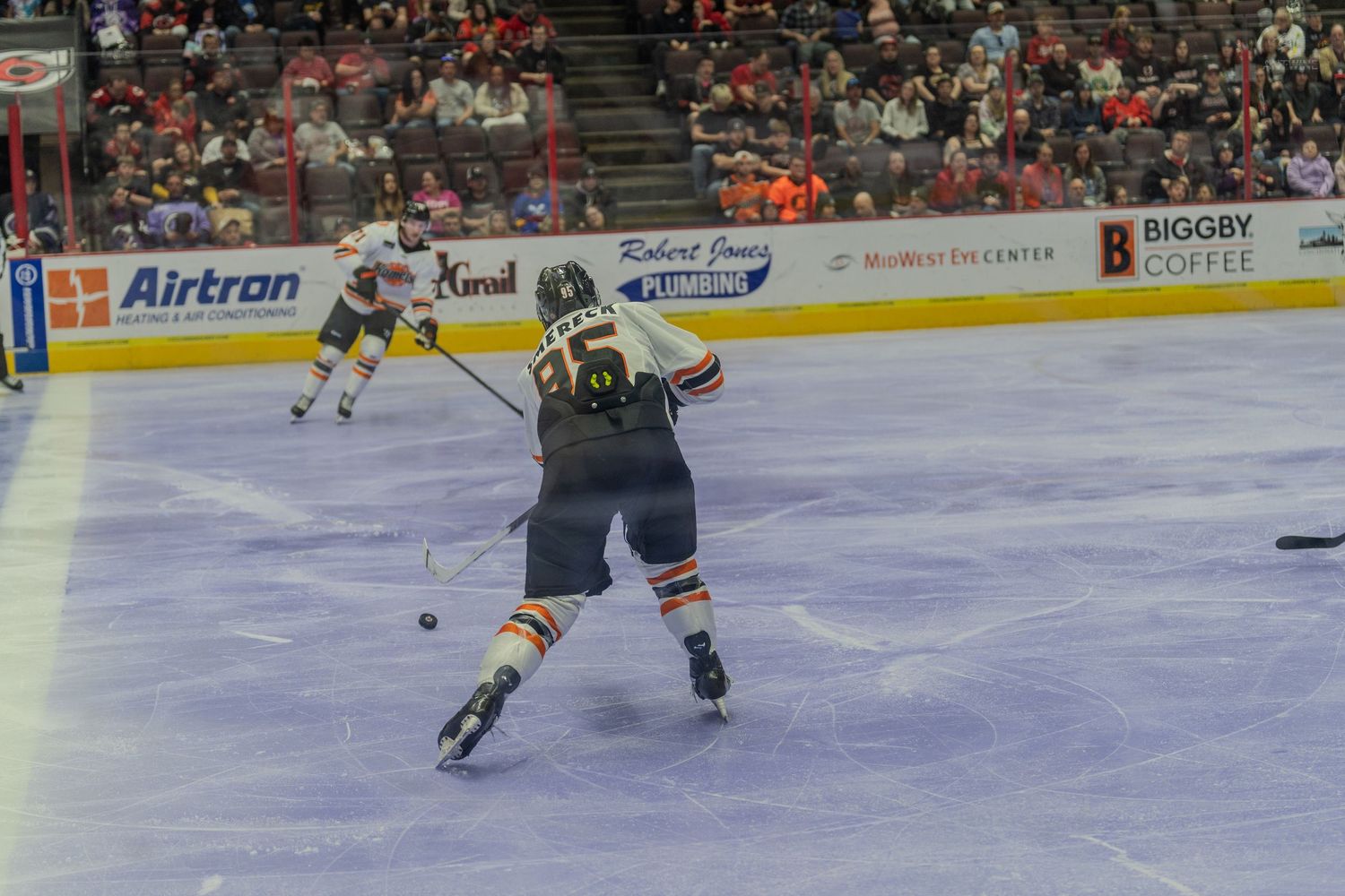 Hockey player takes a shot on ice during a professional game in a packed arena.
