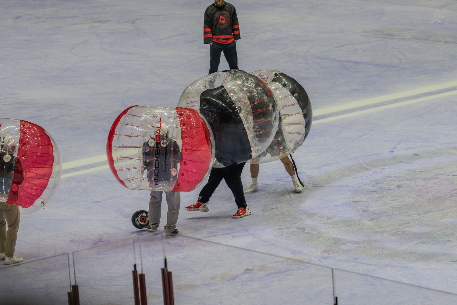 Participants rolling large inflatable bubble soccer balls across an ice rink after a game.