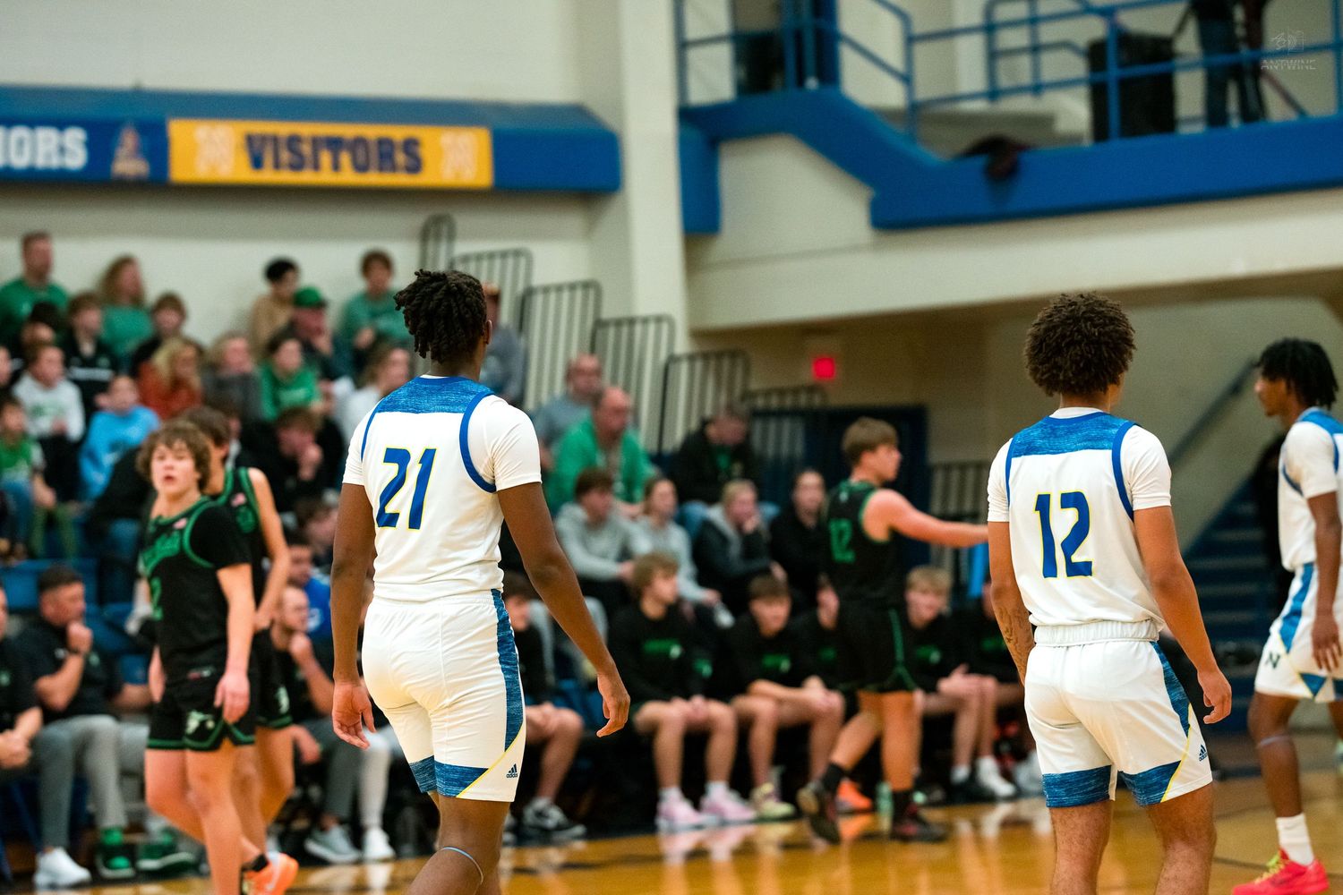 High school basketball players in blue and white uniforms walk on court during an indoor gym game.