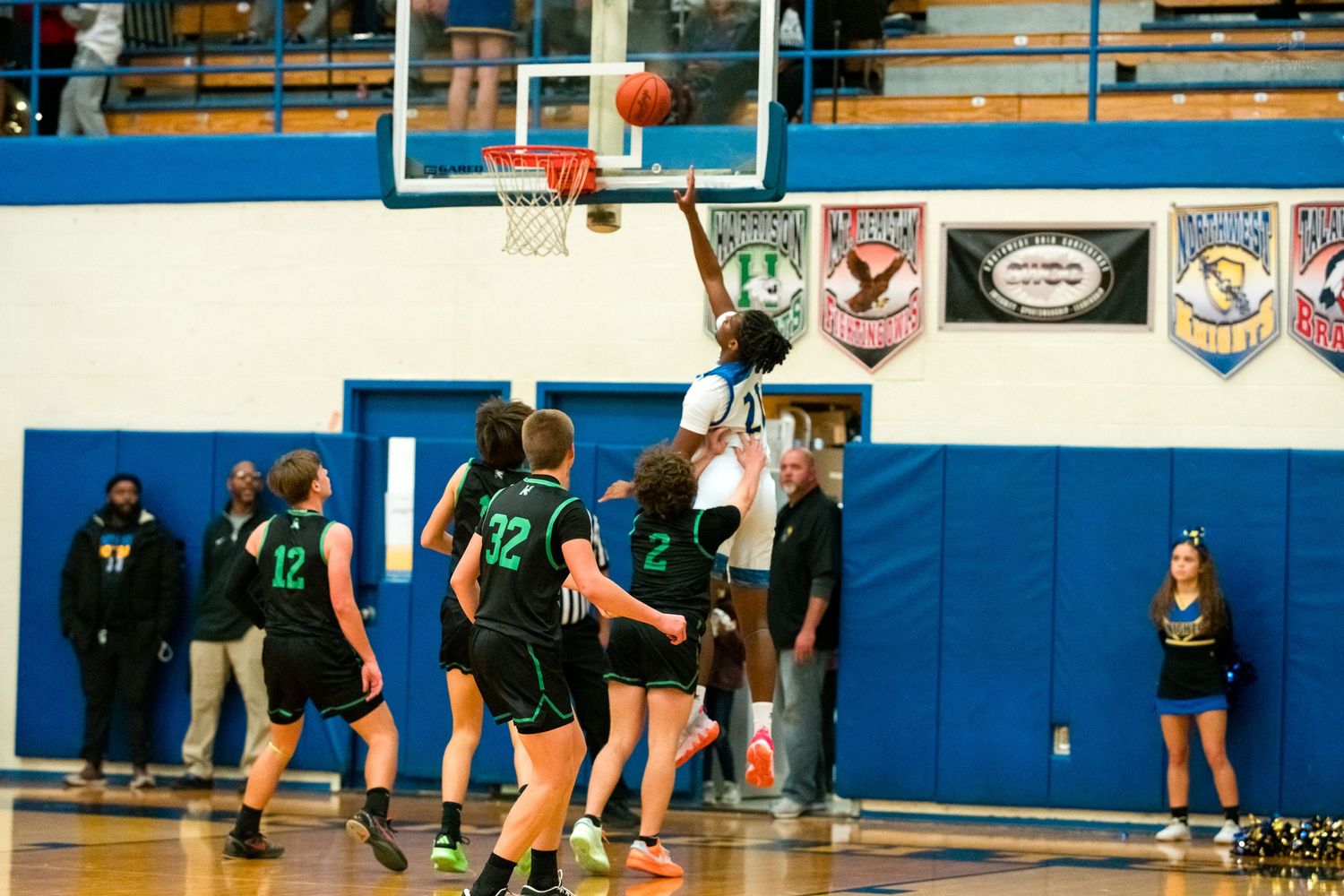 Player attempts layup over defenders in high school basketball game.