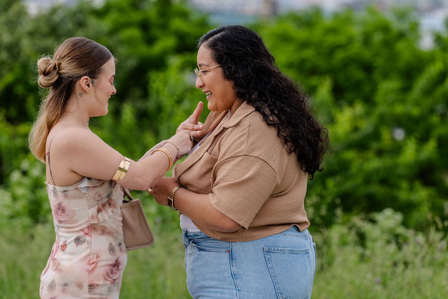 Two women smiling and sharing a joyful moment together in a lush green outdoor setting.