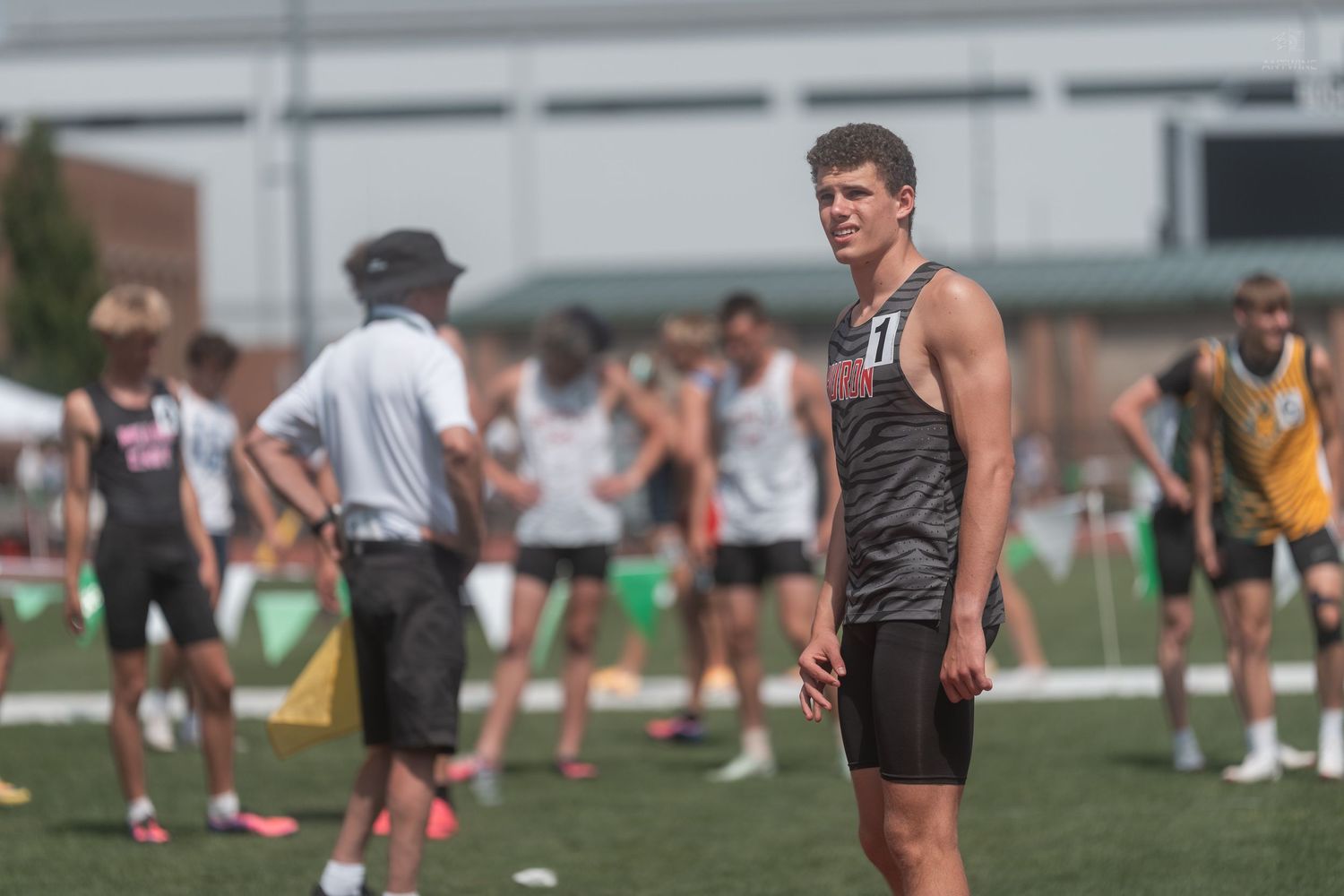 Male track athlete wearing number 11 jersey stands on infield during outdoor track and field competition.
