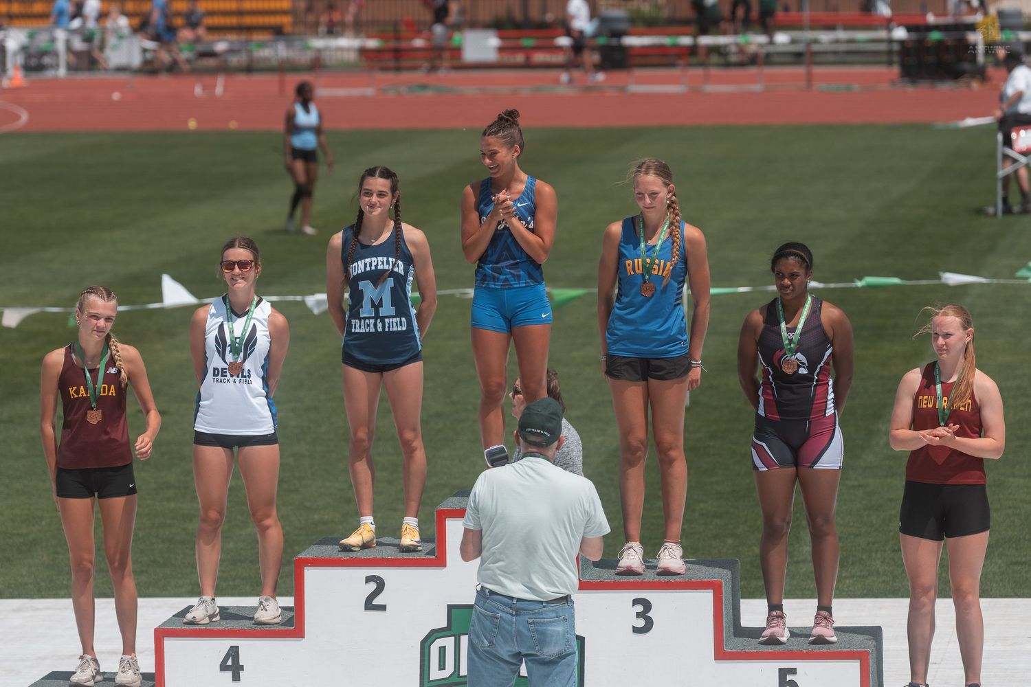 Female athletes stand on the OHSAA awards podium being photographed at a high school state championship.