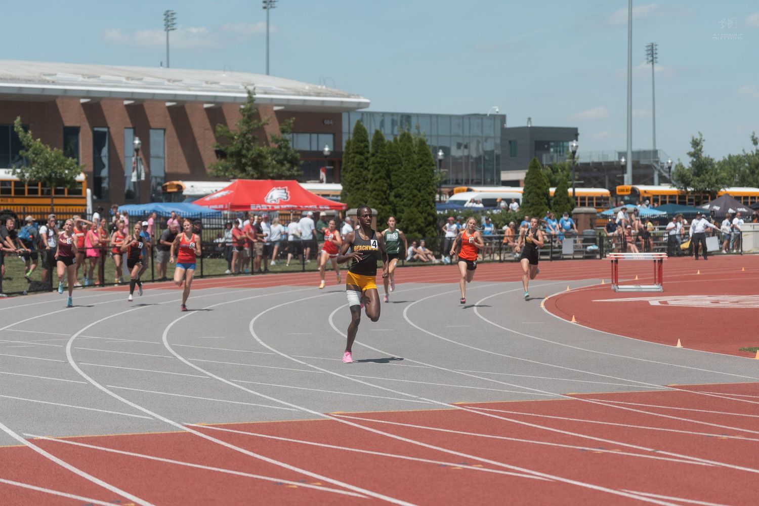 Runners sprinting on red track during outdoor track and field championship competition on sunny day.