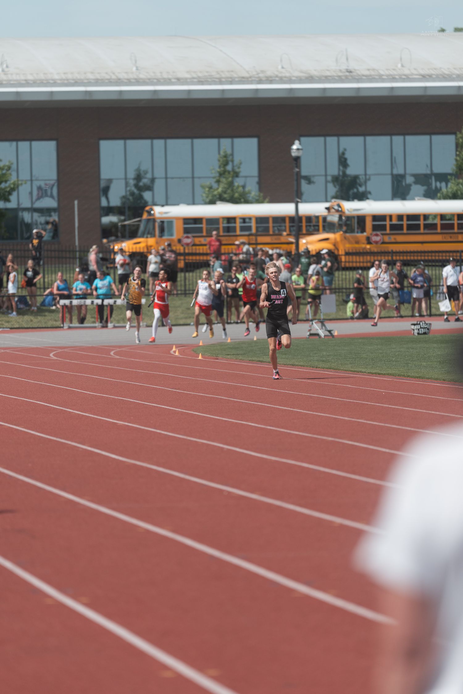 Male athletes compete in a distance race on a red track at a high school track and field meet.