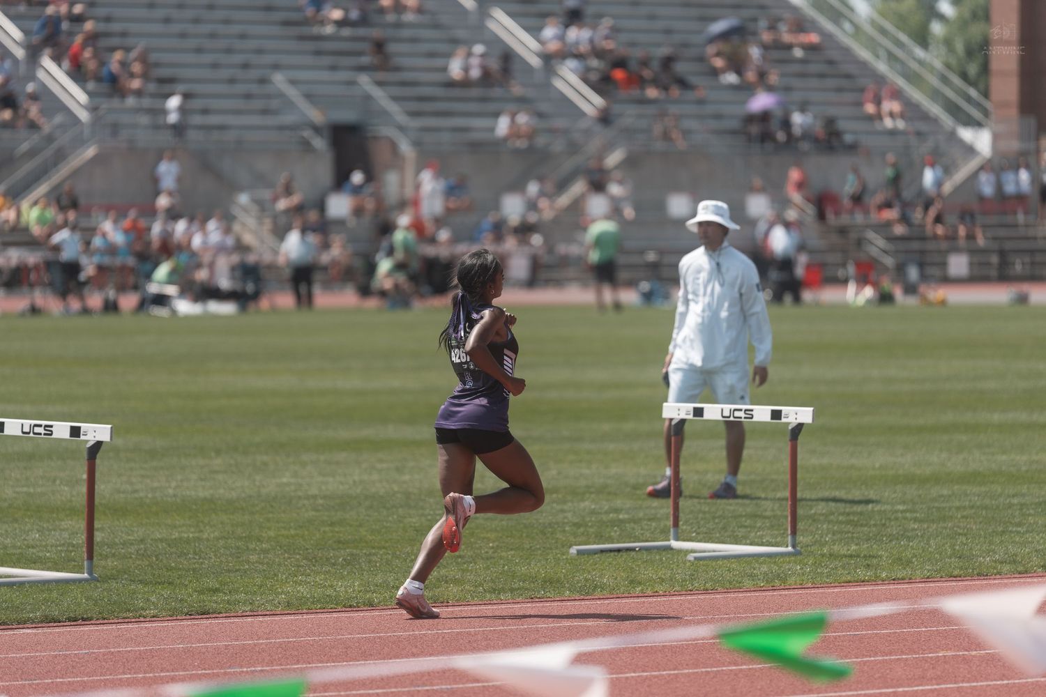 Female sprinter passing hurdle on track at outdoor collegiate track and field competition.
