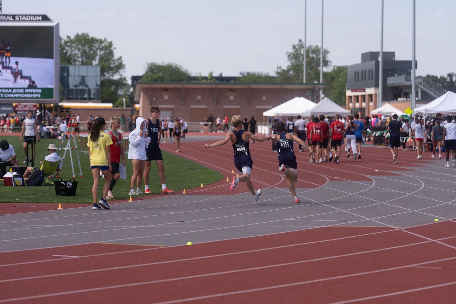 Young athletes race on red track at outdoor track and field competition near stadium.