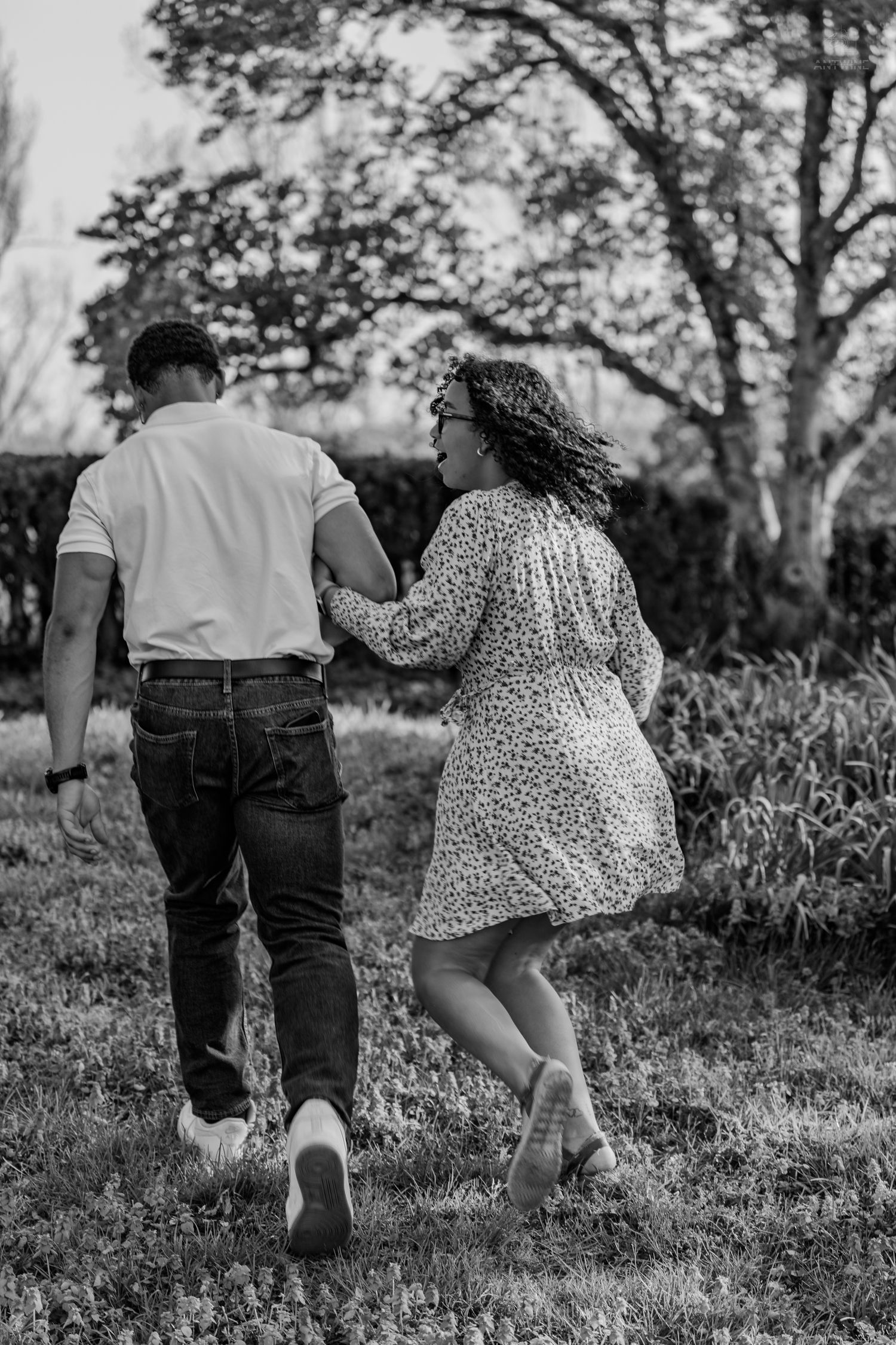 A couple walking together through a lush green park, the woman in a floral dress laughing joyfully.