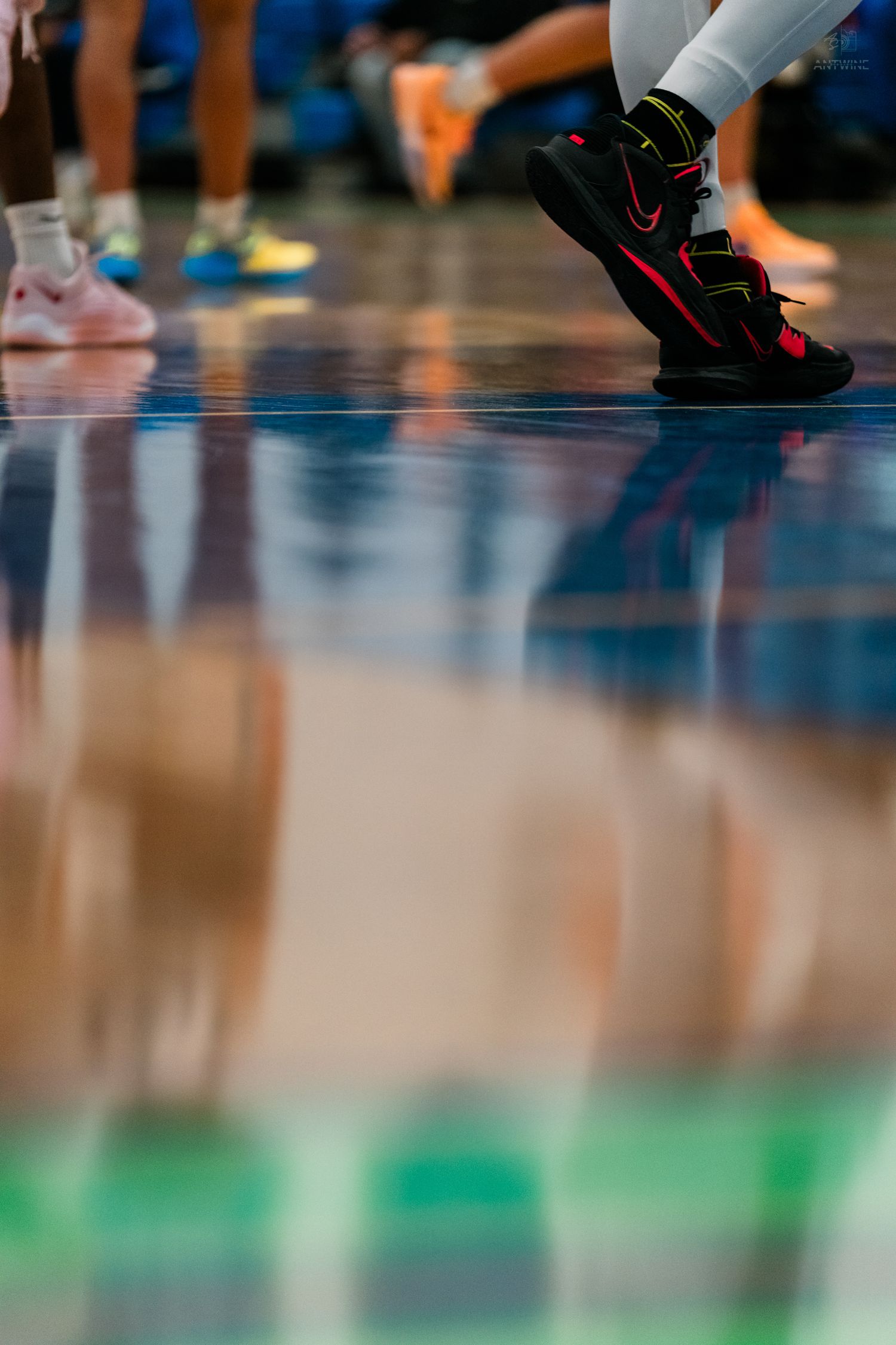 Close-up of a player wearing black and red Nike high-top sneakers reflecting on a polished basketball court.