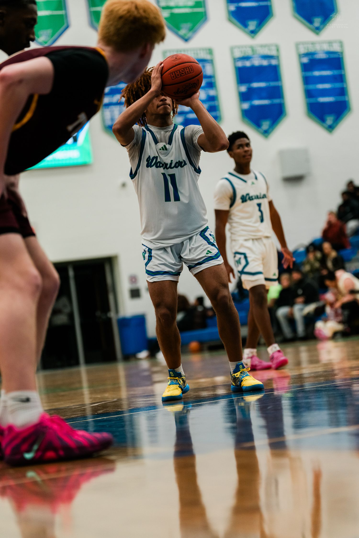 Warriors player number 11 attempts a free throw shot during a competitive high school basketball game.