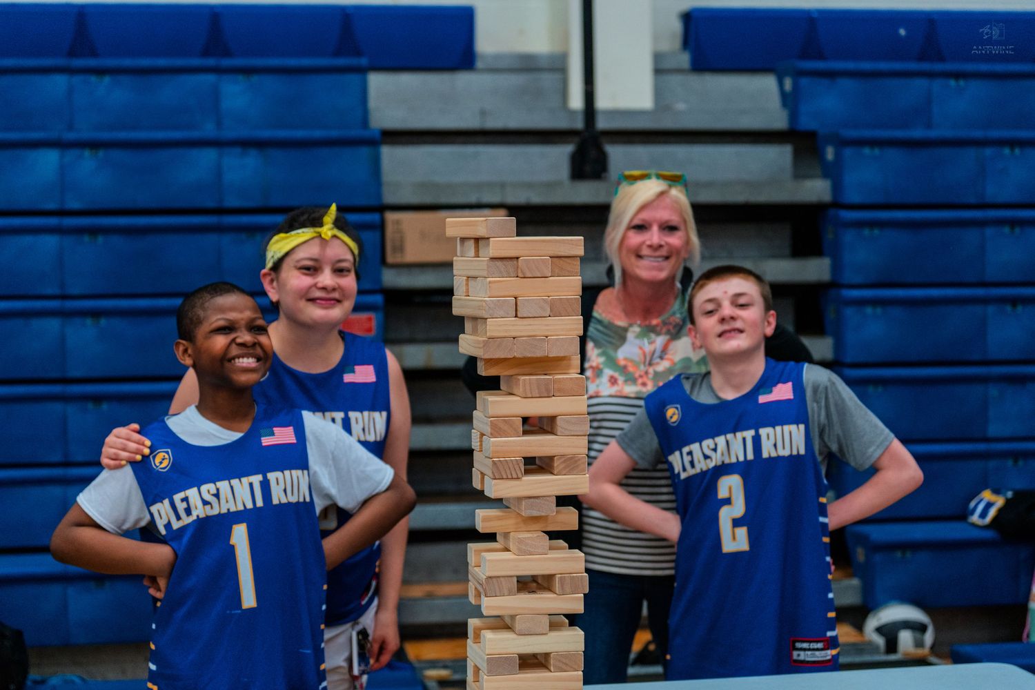 Pleasant Run youth basketball players and adults smile together next to a tall Jenga tower in a gymnasium.