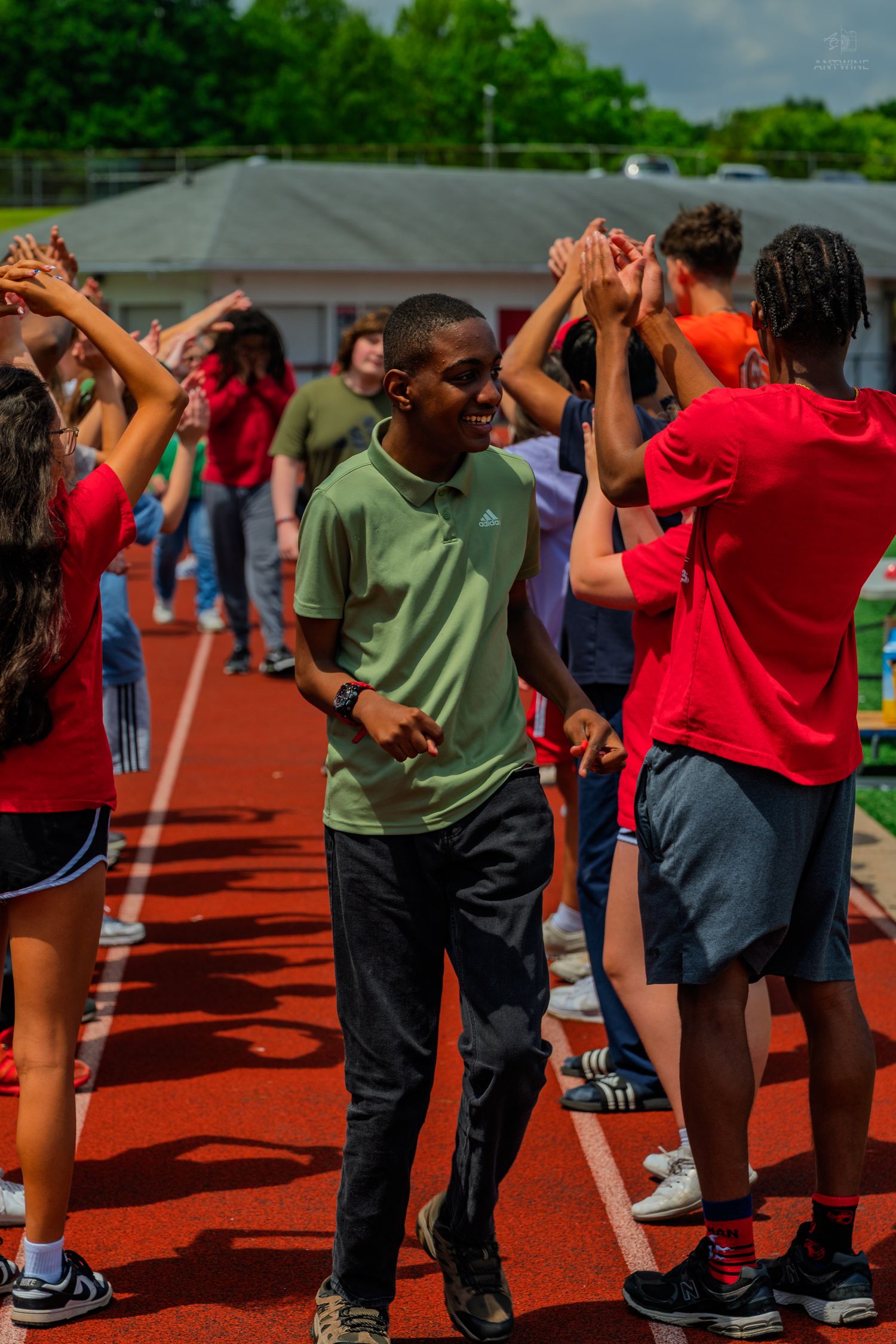 Students high-fiving on a red track during an outdoor school event on a sunny day.