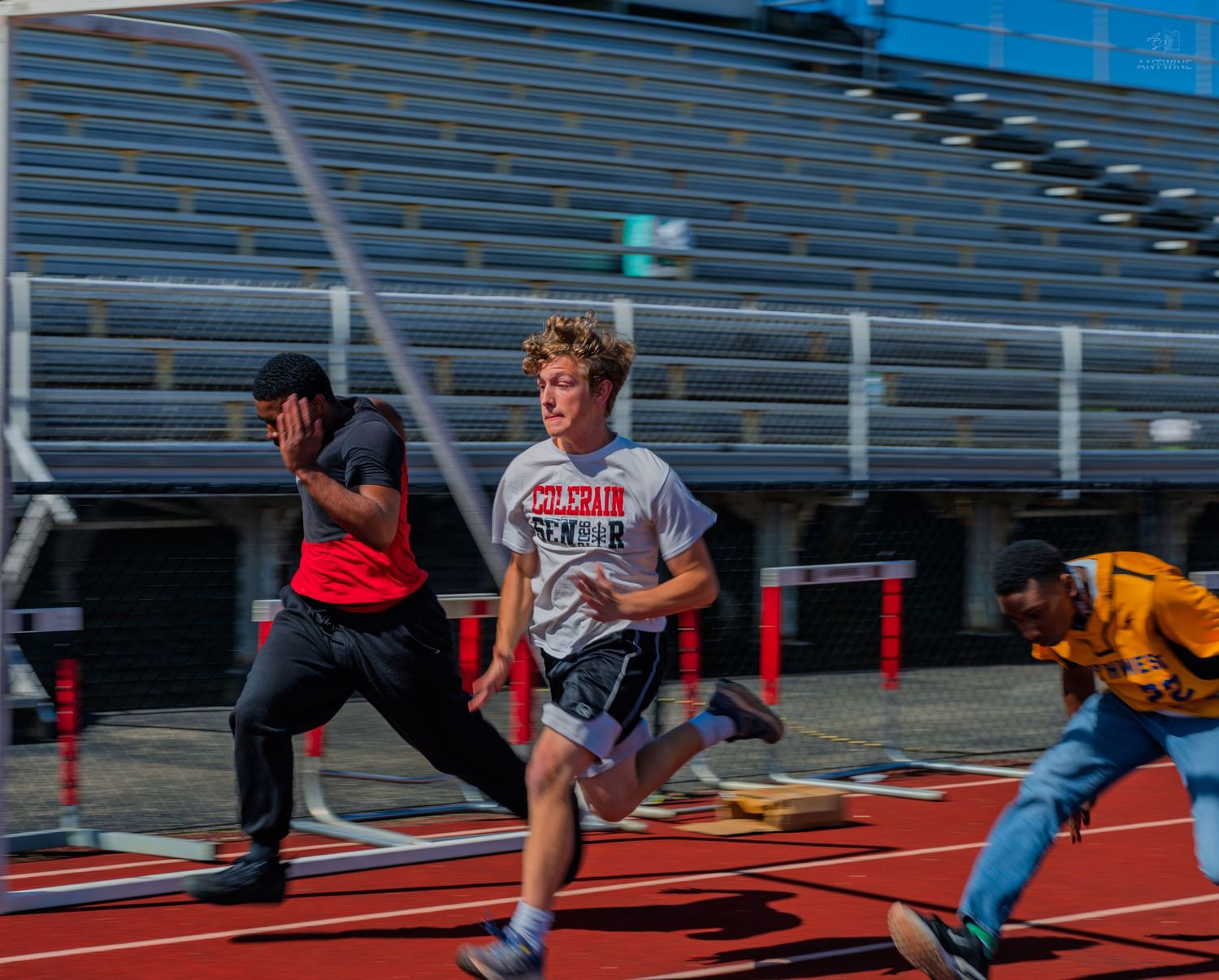 Three athletes sprint on a red track in a stadium during a competitive race event.