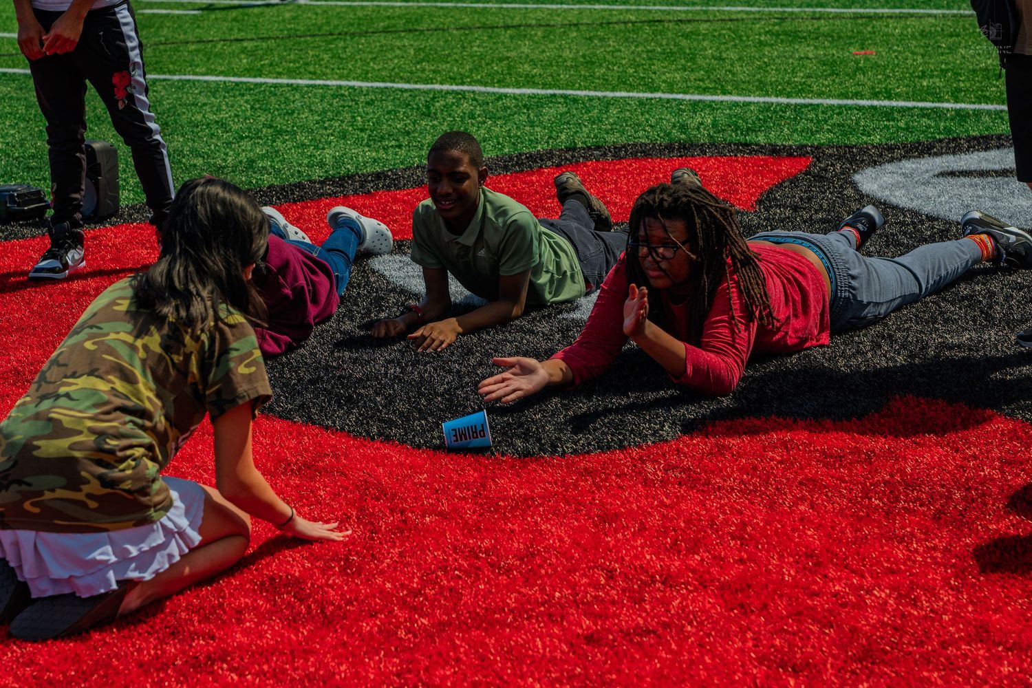 Children playing and lying on red and black artificial turf field on a sunny day.
