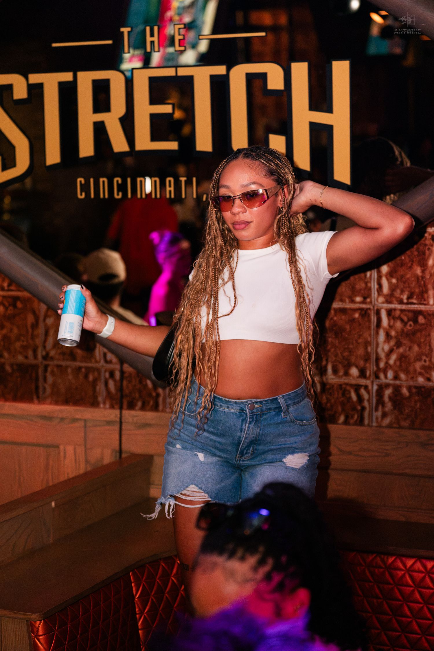 A woman with long braids poses in a white crop top at The Stretch Cincinnati bar.
