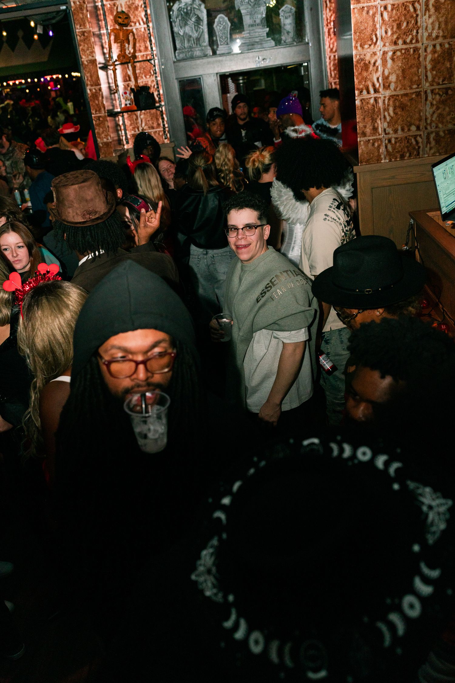 Crowded Halloween party with diverse guests in costumes socializing inside a dimly lit bar venue.