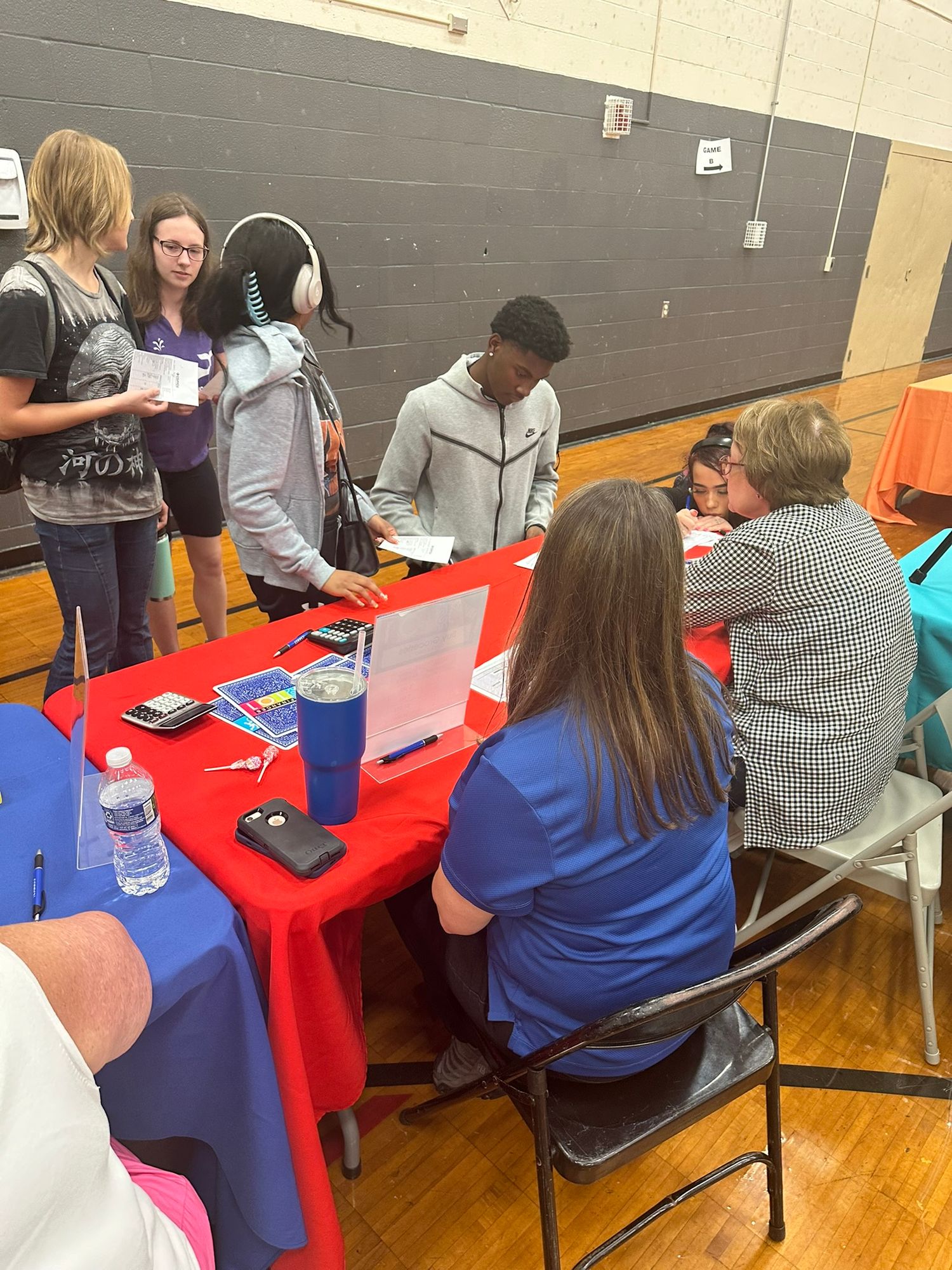 Students and adults interact at colorful tables during a school financial literacy or career fair event.