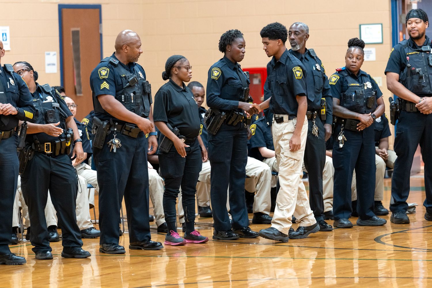 Police officers in uniform standing in a line during an indoor ceremony on a basketball court.