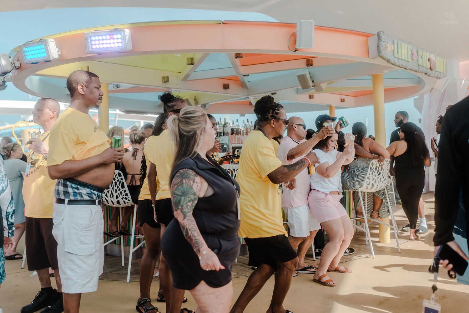 Diverse group of people dancing at an outdoor bar on a cruise ship deck.