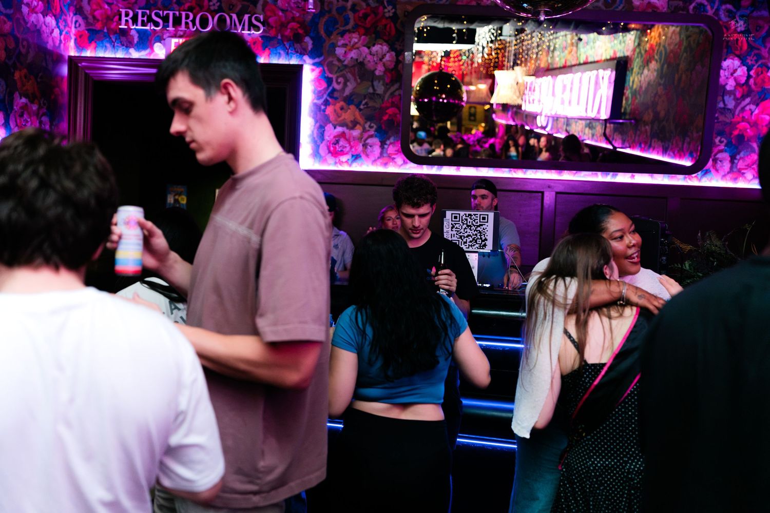 Young adults socializing near restrooms in a vibrant neon-lit nightclub.