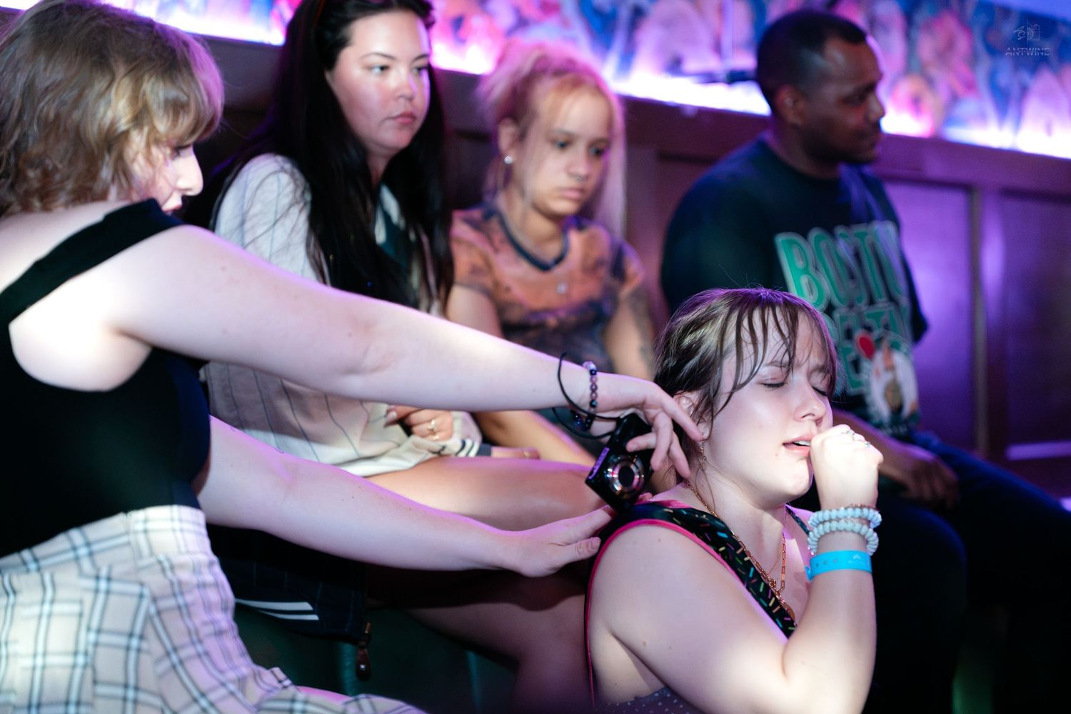 Group of friends at a nightclub with one woman adjusting anothers collar accessory.