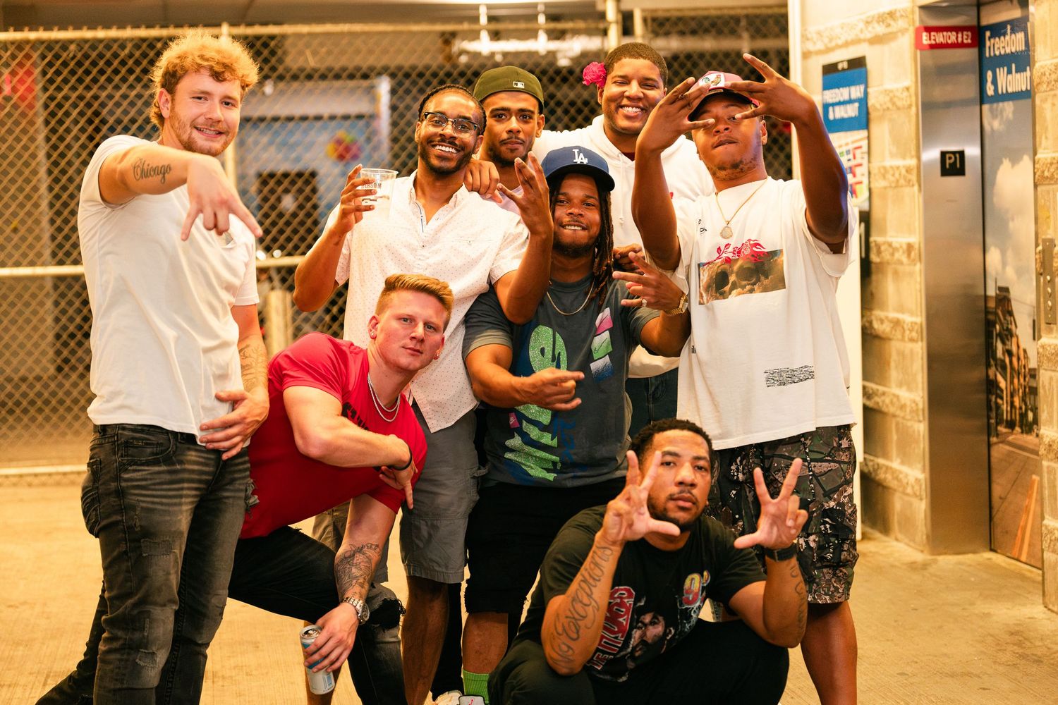 Large group of friends posing together indoors, smiling and making hand gestures.