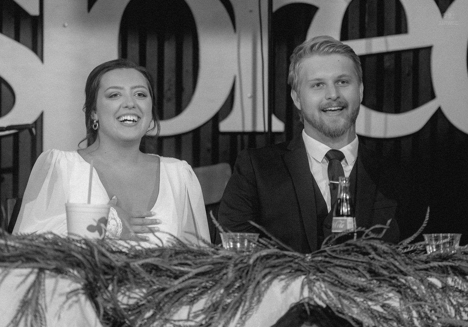 Black and white portrait of a smiling bride and groom seated together at their wedding reception.