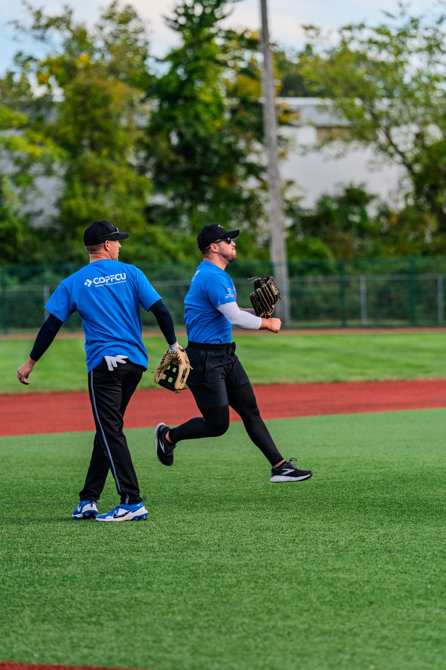 Two players in blue uniforms with baseball gloves jog across a green turf field during a game.