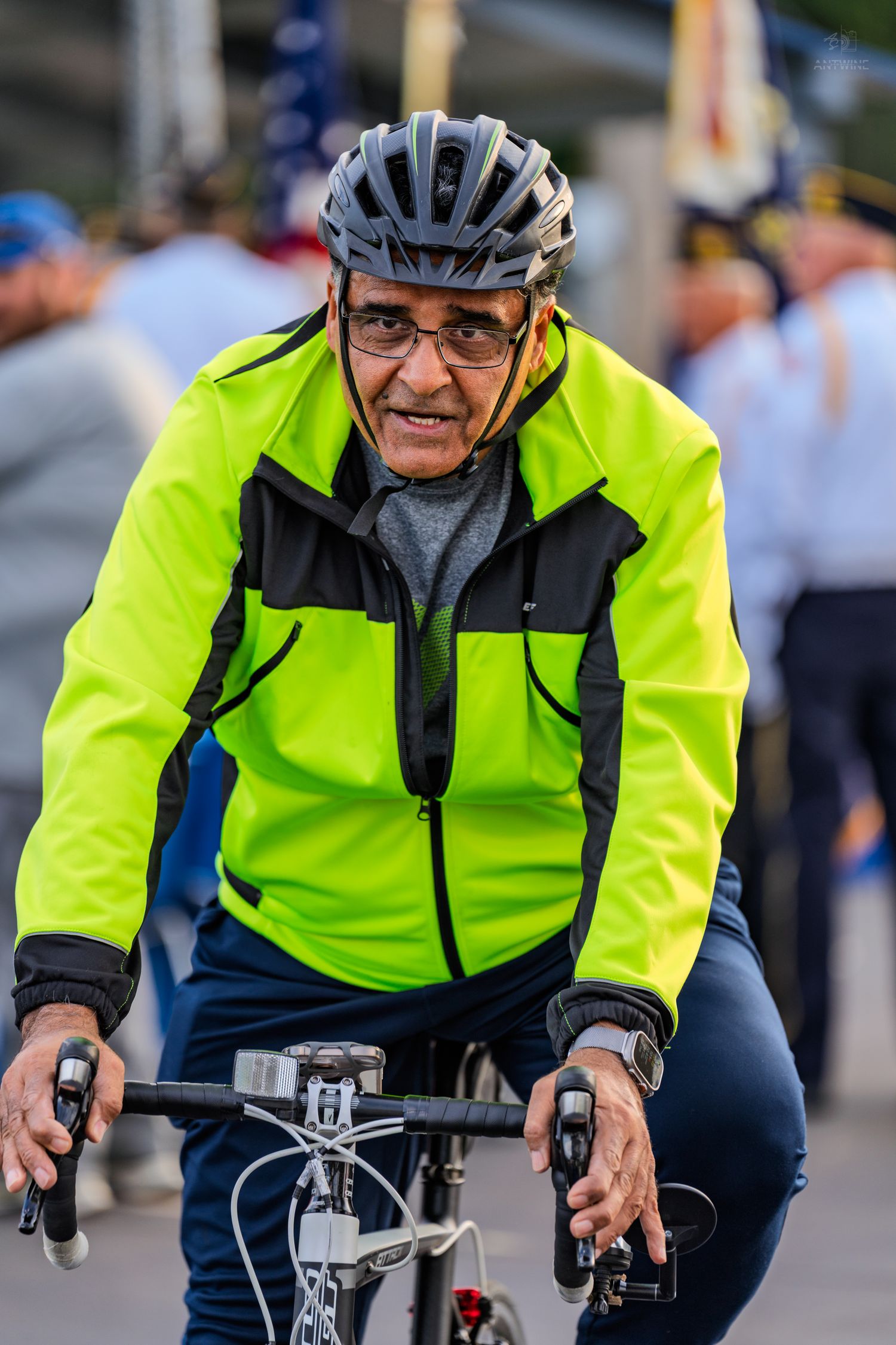 Senior cyclist in neon yellow jacket and helmet riding bicycle outdoors.