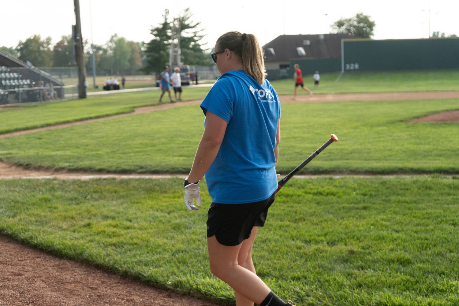 Woman in blue t-shirt holding a baseball bat on a green baseball field during an outdoor game.