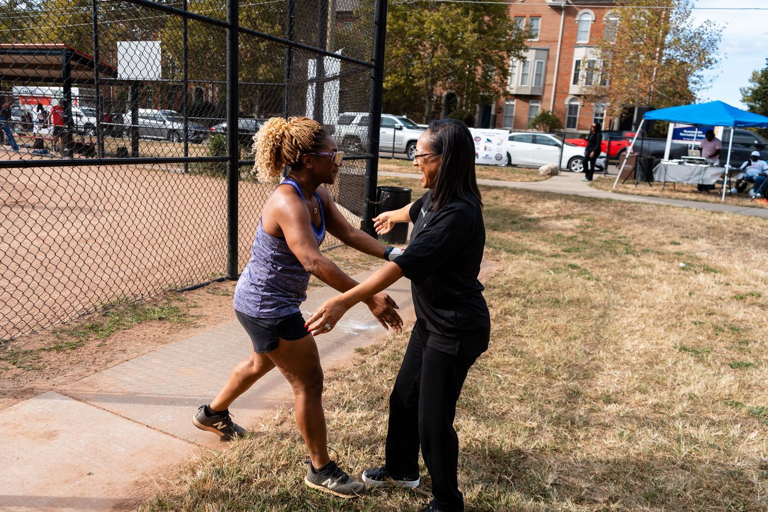 Two women practicing self-defense moves outdoors near a chain-link fence in a park setting.