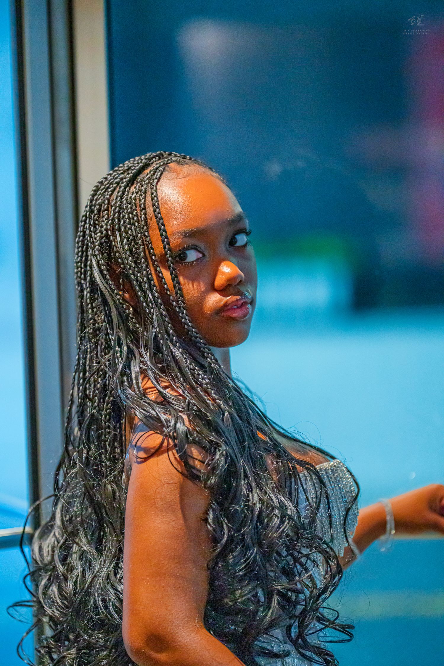 Young woman with long braided hair in a sparkling dress gazing sideways in a blue-lit setting.
