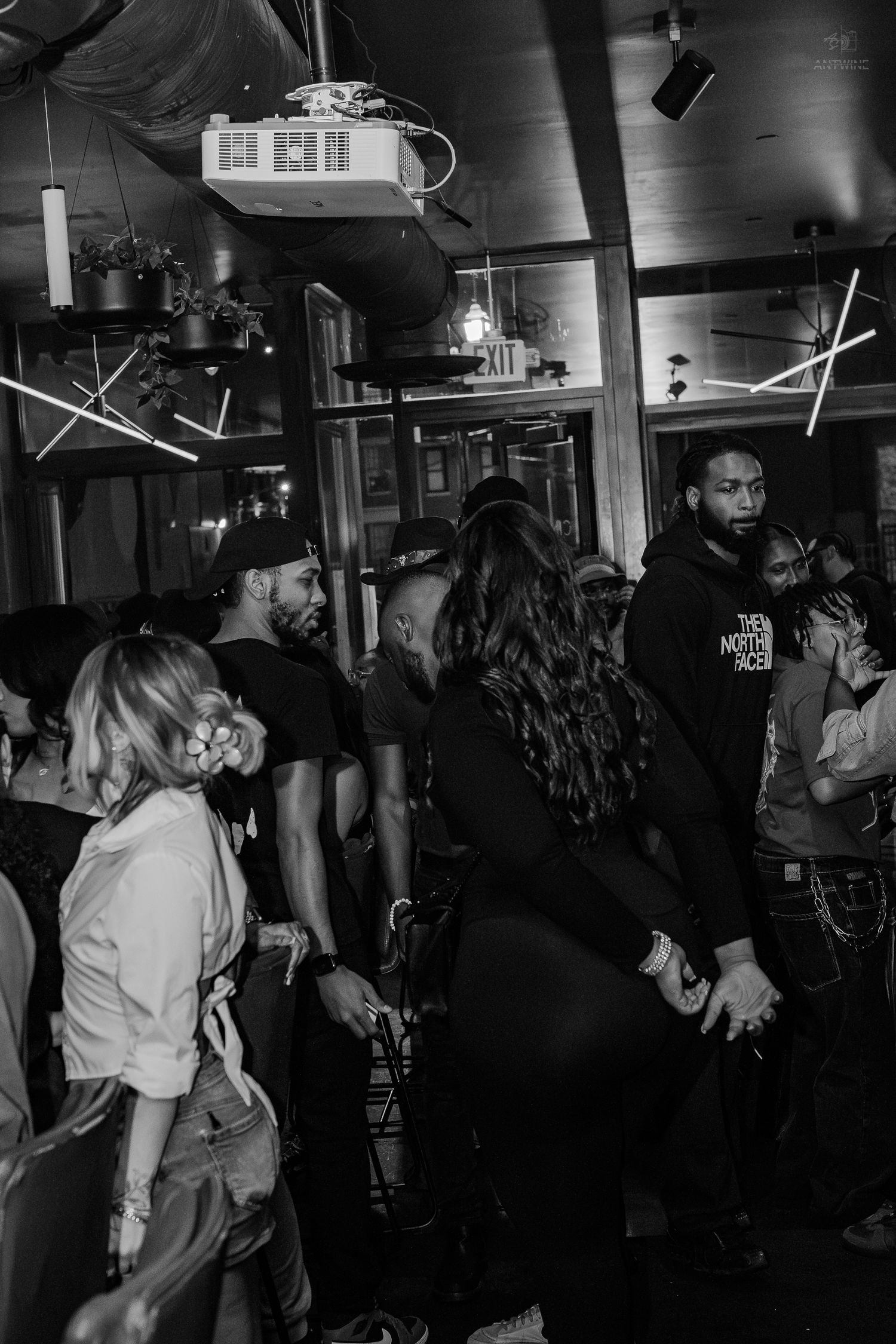 Black and white photo of a lively indoor party with guests socializing under neon lights.