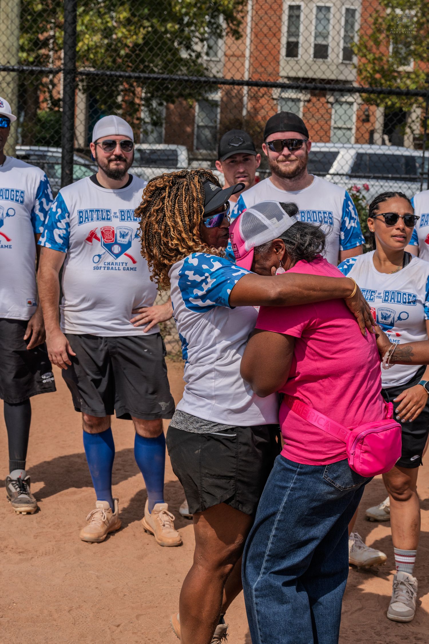 Charity softball team members watch emotional embrace between player and fan on field.