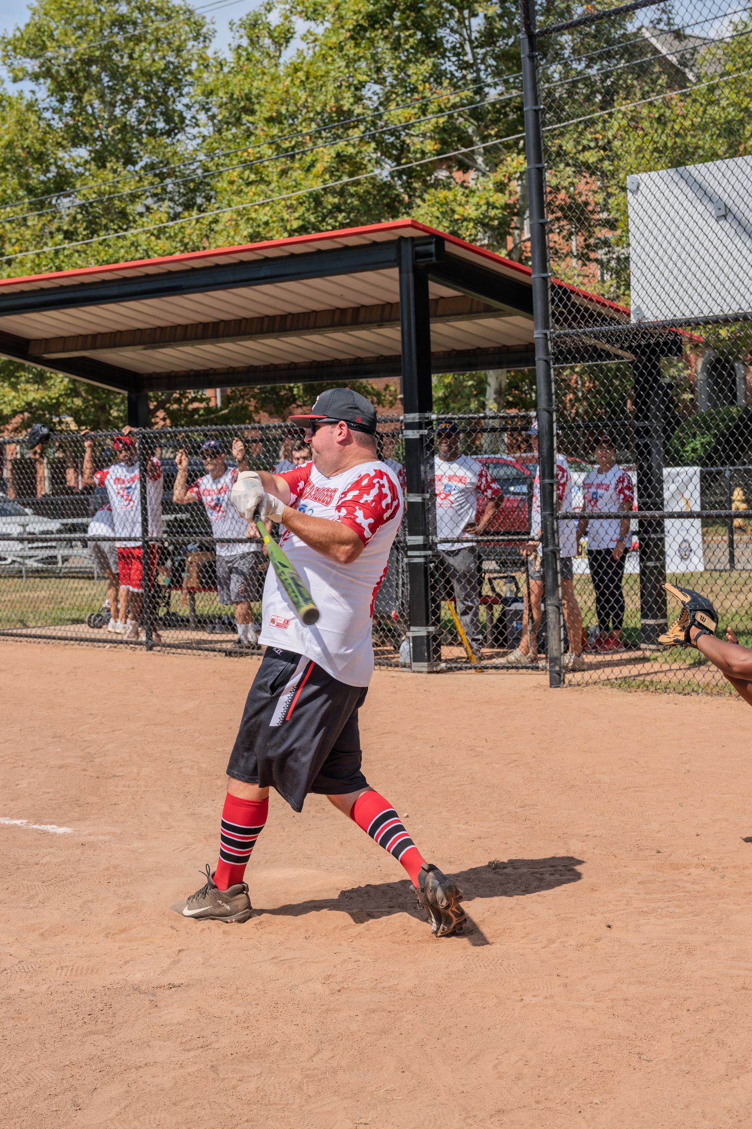 Male softball player swinging bat at outdoor baseball diamond during game.